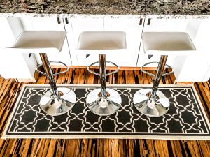 Throw rug below three bar stools at a granite countertop